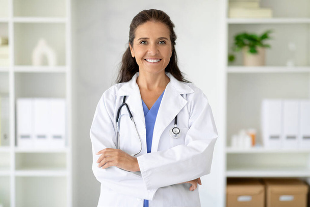 Private medical practice. Portrait of friendly smiling beautiful long-haired middle aged woman wearing medical coat doctor posing at clinic, smiling at camera. Medical staff, healthcare - Photo, Image