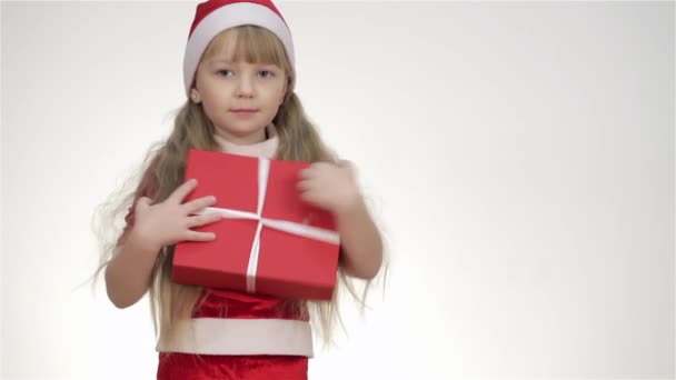 Baby girl, kid, child in Santa hat posing in a studio. Isolated on a white background. Offers, gift, looking at the clock, shows the copyspace, look at copy place , making shhh, hugging a teddy bear - Footage, Video
