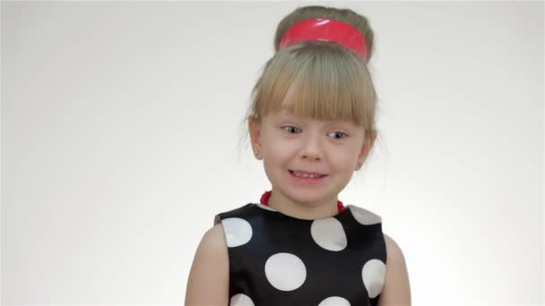 Kid girl posing in studio isolated on white background. The girl in the summer red polka dot sleeves and arm warmers, hair ribbon. She is surprised, looks on copy space, threatens finger, shouting - Footage, Video