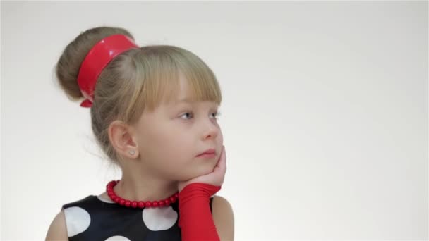 Kind meisje poseren in studio geïsoleerd op witte achtergrond. Het meisje in de zomer rode polka dot mouwen en armwarmers, haarlint. Ze is verrast, kijkt naar kopieerruimte, bedreigt vinger, schreeuwt - Video