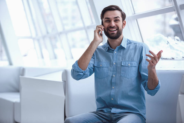 Hombre de negocios guapo está hablando en el teléfono móvil y sonriendo mientras está de pie en la oficina
 - Foto, imagen