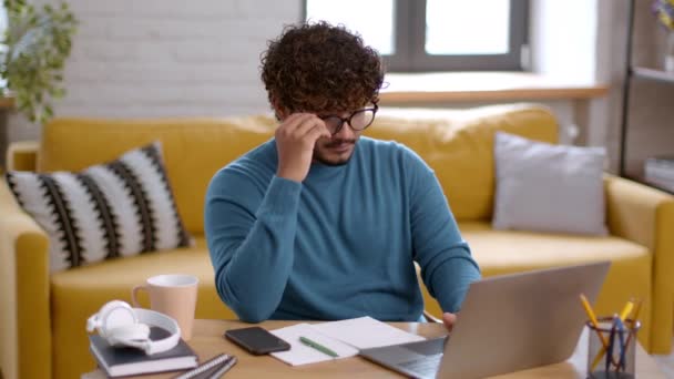 Concept de surcharge de travail. Jeune homme indien tapant sur ordinateur portable au bureau à la maison et se sentant fatigué, enlevant les lunettes et massant son nez pont, se sentant épuisé de l'écran numérique - Séquence, vidéo