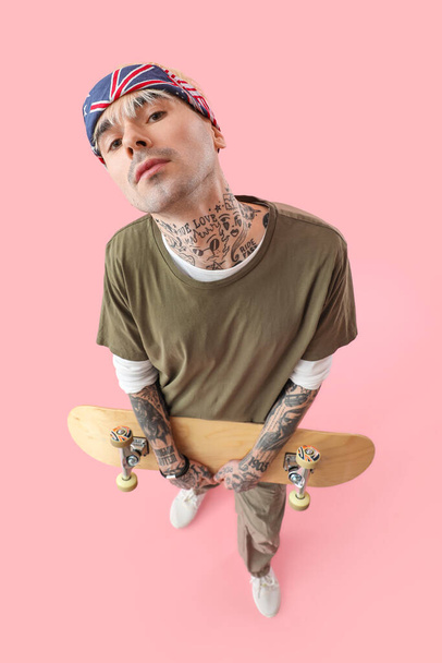 Tattooed young man with skateboard on pink background - Photo, Image