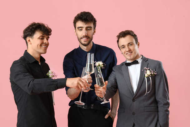 Młodzi mężczyźni ubrani na bal z kieliszkami szampana na różowym tle - Zdjęcie, obraz