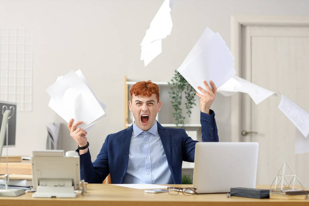 怒っている赤毛の実業家は,オフィスのテーブルに紙を投げます - 写真・画像