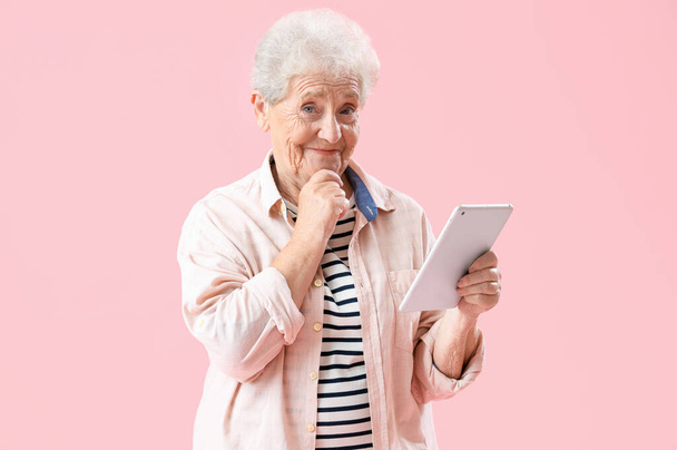 Ragionevole donna anziana utilizzando tablet computer su sfondo rosa - Foto, immagini