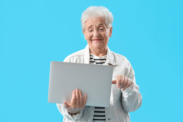 Donna anziana che utilizza il computer portatile su sfondo blu - Foto, immagini