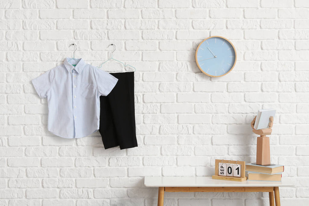 Mesa com calendário, relógio e uniforme escolar elegante pendurado na parede de tijolo leve no quarto - Foto, Imagem