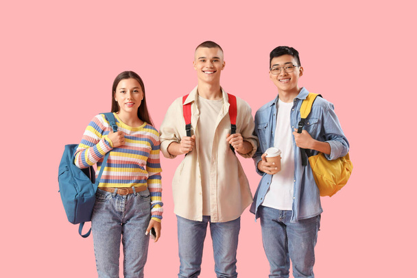 Gelukkige studenten met rugzakken en een kop koffie op roze achtergrond - Foto, afbeelding