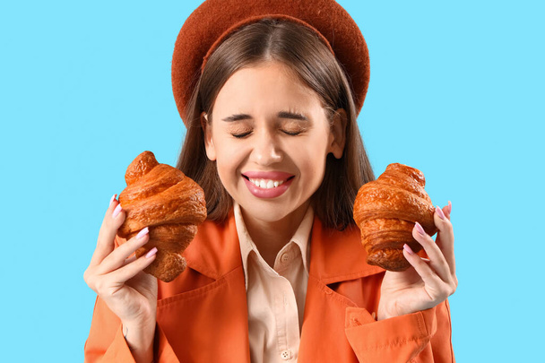Mooie gelukkige jonge vrouw in baret met lekkere croissants op blauwe achtergrond - Foto, afbeelding
