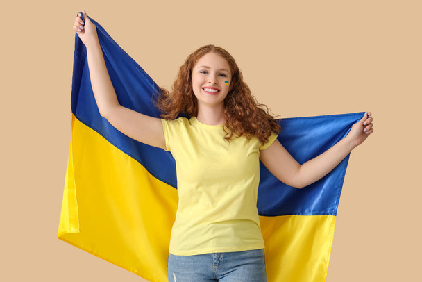 Feliz hermosa mujer joven con bandera de Ucrania sobre fondo beige - Foto, Imagen