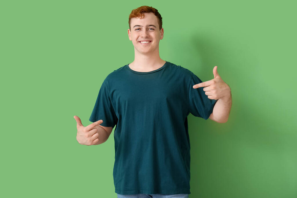 Giovane uomo che indica la sua t-shirt su sfondo verde - Foto, immagini