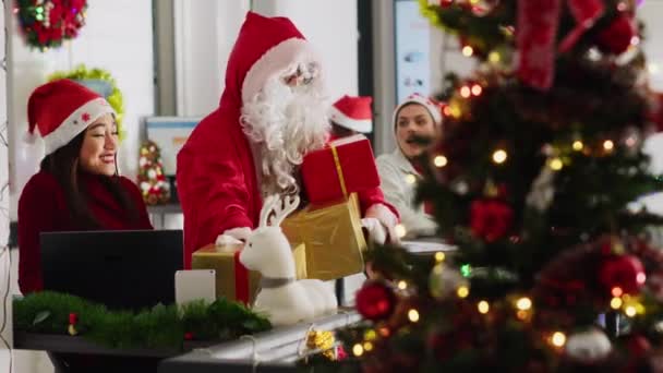 Multiethnische arbeiders die geschenken ontvangen van collega die zich voordoet als kerstman in een kerstversierd kantoor. Werknemer draagt kostuum verrassend personeel met geschenken tijdens de wintervakantie - Video