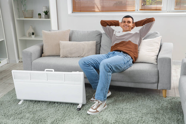 Hombre joven calentando cerca del radiador en casa - Foto, Imagen