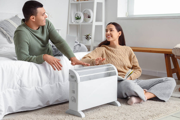 Jeune couple se réchauffant les mains près du radiateur dans la chambre - Photo, image