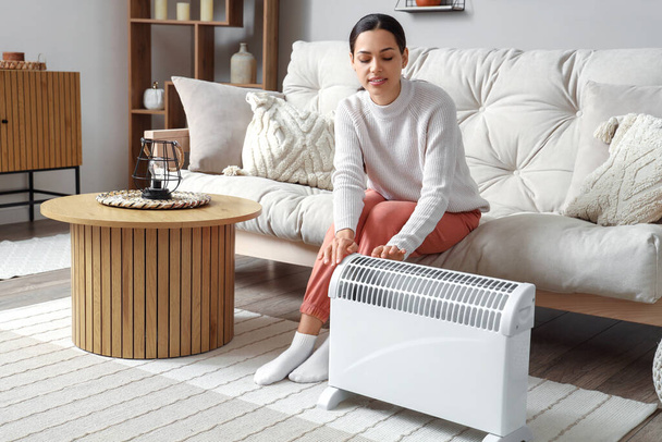 Mujer joven calentándose cerca del radiador en casa - Foto, imagen