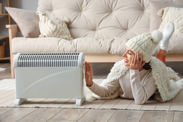 Jeune femme avec chauffage à carreaux près du radiateur à la maison - Photo, image