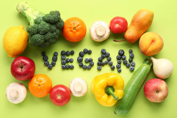 緑の背景に異なる果物や野菜とブルーベリーで作られたWord VEGAN - 写真・画像