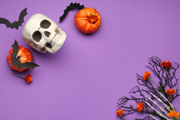 Halloween composition with skull, pumpkins, skeleton hand and marigold flowers on purple background - Photo, Image
