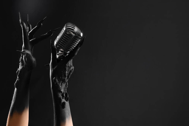 Manos de bruja con micrófono sobre fondo negro. Halloween celebración - Foto, Imagen