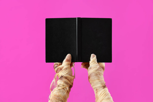 Mummy hands with hardcover book on pink background. Halloween celebration - Photo, Image