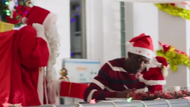 Pracovník, který dostává dárky od kolegy oblečeného jako Santa Claus v ozdobném pracovním prostoru. Převlečený spolupracovník překvapující nic netušící veselý zaměstnanec s dárky před vánoční kancelářské slavnosti - Záběry, video