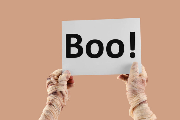Mami manos sosteniendo hoja de papel con texto BOO sobre fondo beige. Halloween celebración - Foto, imagen