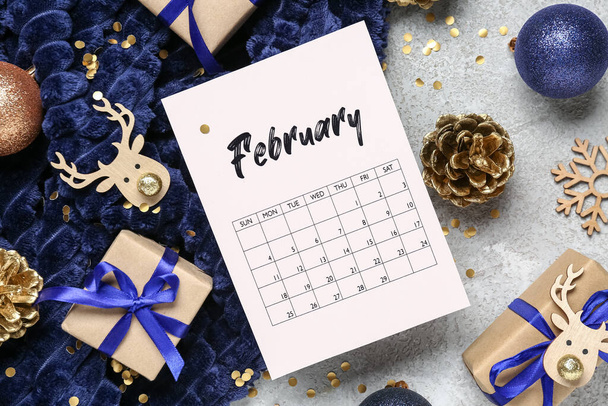 Paper calendar for February, gift boxes and Christmas decorations on grey background - Photo, Image