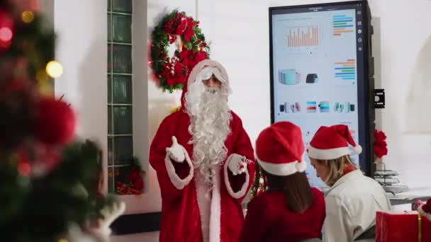クリスマスシーズンにサンタとして服を着たマネージャーがチームミーティングを開催し,来年のデジタルスクリーン戦略を示した. 従業員と話すお祝いの装飾オフィスのチームリーダー - 映像、動画