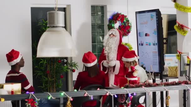Gerente vestido de Papai Noel durante a temporada de Natal segurando reunião de equipe, apresentando gráficos financeiros na tela digital. Líder de equipe em escritório decorado festivo motivando os trabalhadores - Filmagem, Vídeo