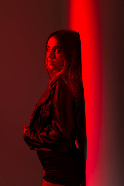 明るい赤い壁に黒い服を着て立っている美しい白人女性. スタジオポートレート - 写真・画像