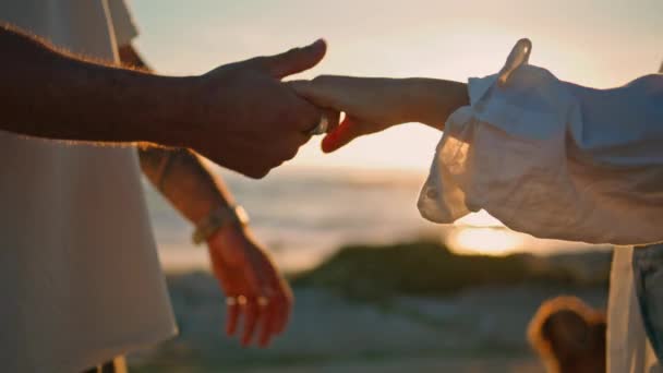 Liefde paar verbinden handen op heldere zon zee strand closeup. Onherkenbaar liefdevolle meisje en man aanraken vingers bij zonsondergang oceaan kust. Zonnige lichten knipperen tussen de armen van mensen. Gevoelens  - Video