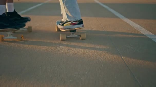 Patinadores de primer plano piernas montando longboards en asfalto carretera. Pareja desconocida disfrutando de tablas de skate paseo rápido en la calle de la ciudad. Milenials activos pasan fin de semana juntos en el terraplén oceánico de verano  - Imágenes, Vídeo