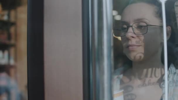 Caucásico atractiva joven mujer con gafas caminando por la puerta de un café - Metraje, vídeo