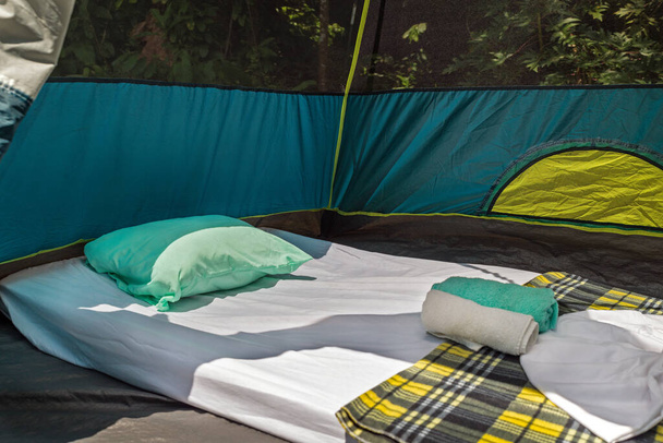 Közelkép egy matrac, párna, lepedő és törölköző belsejében egy sátor az erdőben - Fotó, kép