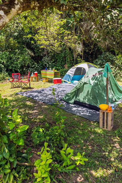 Két sátor kemping a trópusi erdőben székekkel, piknik asztal, ételek és italok, hűvösebb, szappan és törölköző - Fotó, kép