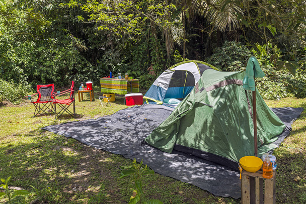 Zeltplatz im tropischen Wald, zwei Zelte, Stühle, Tisch, Essen und Getränke, Kühler, Seife und Handtuch - Foto, Bild