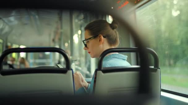 Openbaar vervoer. Vrouw in een bril in de tram met behulp van smartphone chatten en sms 'en met vrienden, achteraanzicht, slow motion. Stad, stad, vervoer. - Video