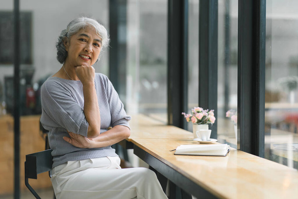Красивая азиатская пожилая женщина с седыми волосами улыбается во время отдыха в кафе - Фото, изображение