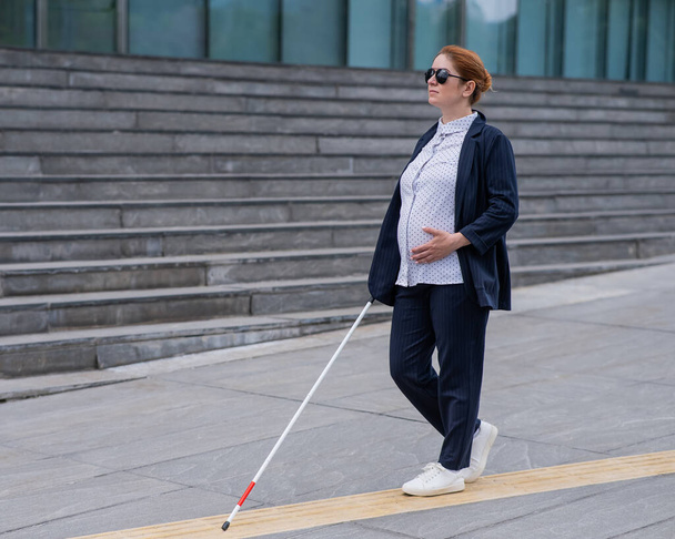 Blind pregnant businesswoman walking along tactile tiles with a cane - Fotó, kép