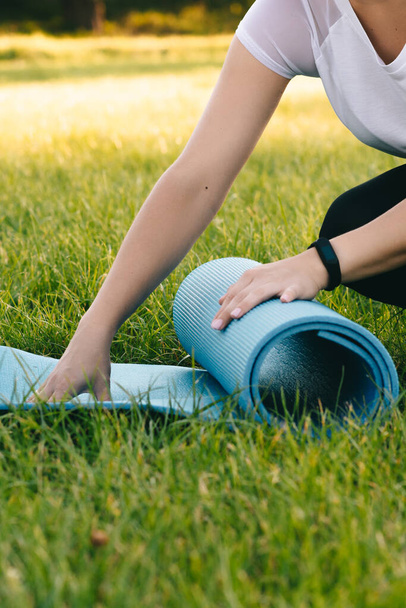 Les mains d'une fille qui déroule un brin d'herbe pour le sport sur la pelouse. Concept de fitness extérieur. Coucher de soleil. - Photo, image