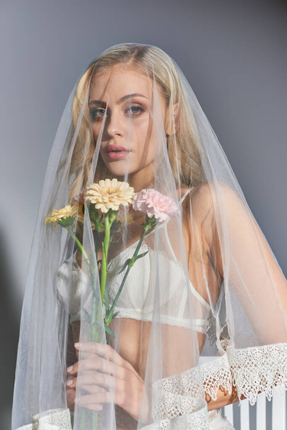 カメラを見ている手の花とポーズをかける魅力的な若い女性の垂直ショット - 写真・画像