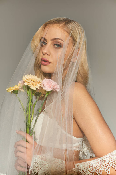 tiro vertical de atraente jovem modelo feminino posando com buquê de flores e olhando para a câmera - Foto, Imagem