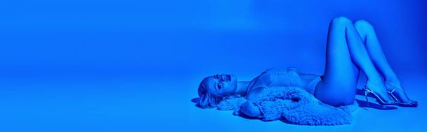 atractiva mujer en lencería erótica y piel sintética tirada en el suelo rodeada de luces azules, pancarta - Foto, Imagen