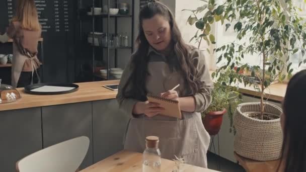 Lassú felvétel fiatal pincérnő Down-szindrómás dolgozik modern kávézó álló asztali írás sorrendben notebook - Felvétel, videó
