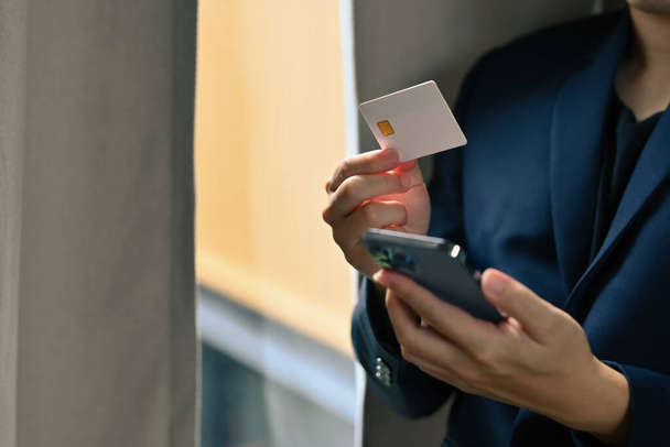 Мужчина держит кредитную карту, совершает транзакцию, оплачивает счета, выставляет счет на смартфон. - Фото, изображение