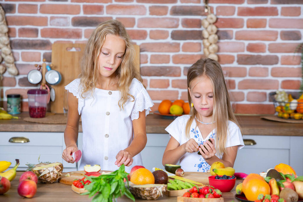 Δύο κοριτσάκια στην κουζίνα με φρέσκα λαχανικά. Υγιεινή διατροφή. Χαρούμενες αδερφές. - Φωτογραφία, εικόνα