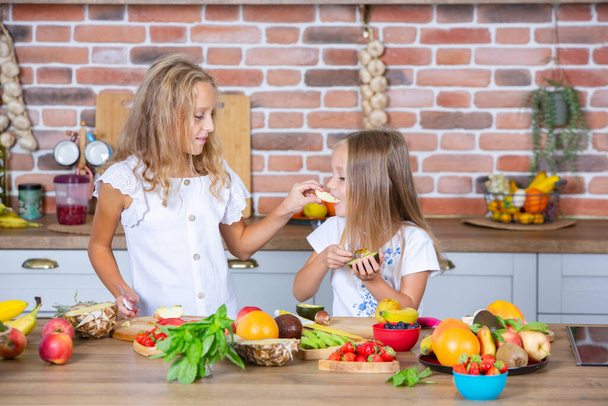 Two little girls in the kitchen with fresh vegetables. Healthy food concept. Happy sisters. - Photo, Image