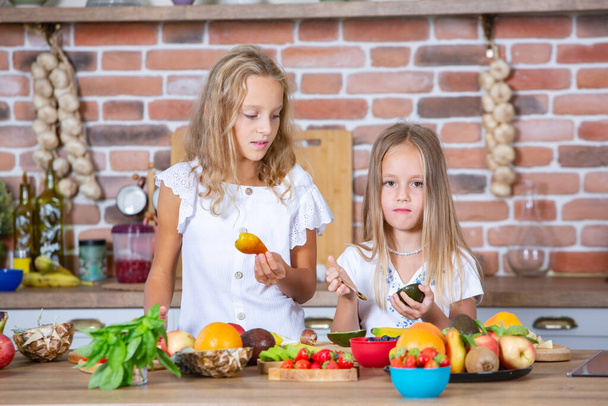 キッチンに2人の小さな女の子が新鮮な野菜を持っています. 健康食品のコンセプト。 ハッピーシスターズ. - 写真・画像