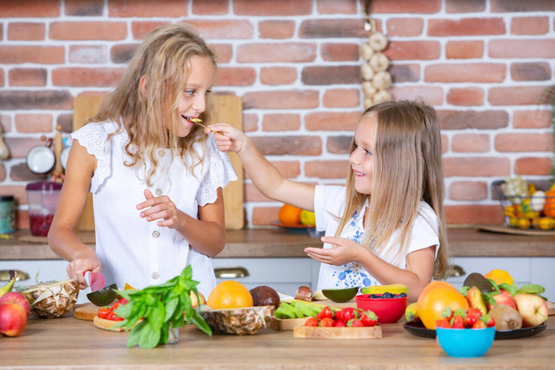 キッチンに2人の小さな女の子が新鮮な野菜を持っています. 健康食品のコンセプト。 ハッピーシスターズ. - 写真・画像